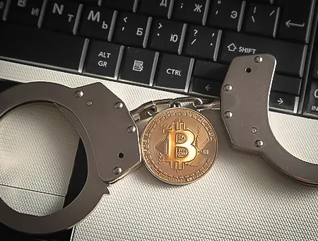 Handcuffs beside a Bitcoin coin on a laptop